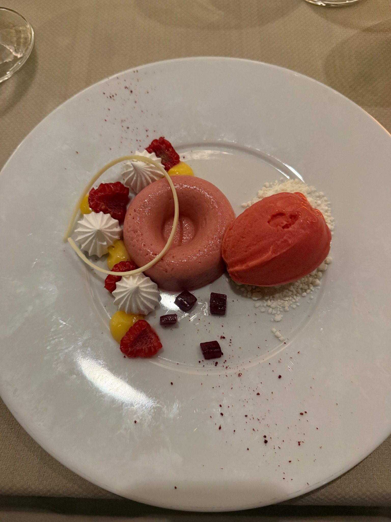 A pink ring-shaped dessert beside a red scoop, with red fruit and white decorations.